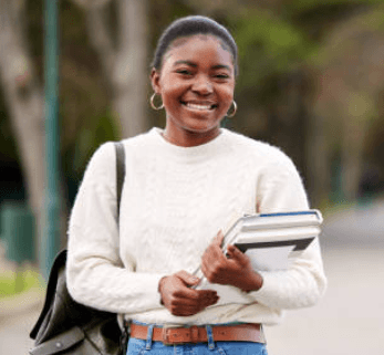 Joven estudiante sonriente con suéter blanco y mochila, sosteniendo libros en un entorno universitario.